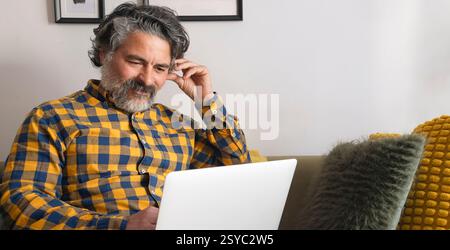 Smiling mature man using laptop on sofa at home Stock Photo