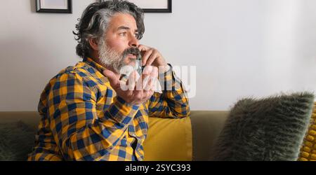 Bearded man gesturing while talking on smartphone at home Stock Photo