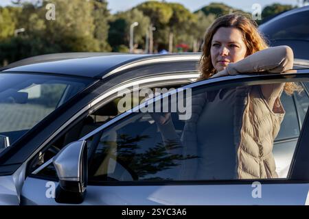 Young woman leaning on the open car door looking into the distance Stock Photo