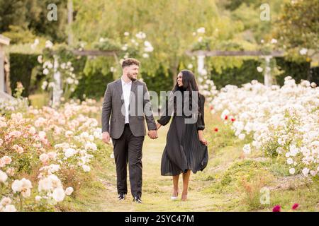 A couple walks hand in hand through a romantic rose garden Stock Photo