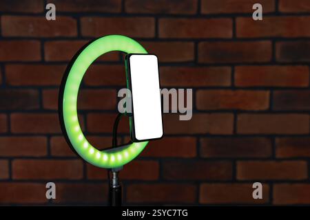 Ring lamp with smartphone against brick wall, closeup. Space for text Stock Photo