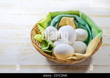 Fresh white eggs for the Easter holidays in a basket with green and yellow cloth on rustic, light-colored wood, copy space, selected focus, narrow dep Stock Photo