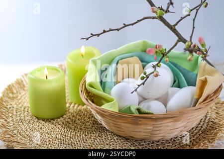 White eggs for Easter holidays in a small basket with a napkin, green candles and a blooming quince branch, copy space, high angle view from above, se Stock Photo
