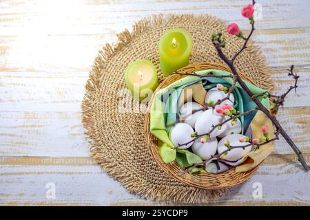 Easter arrangement with white eggs in a basket with a napkin, green candles and a blooming quince branch, copy space, high angle view from above, sele Stock Photo