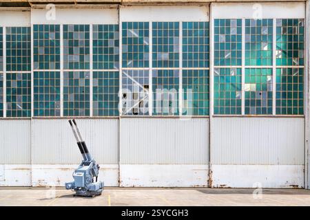 Silver gun is sitting in front of a white wall. The gun is a cannon. The wall is white and has a few cracks in it Stock Photo