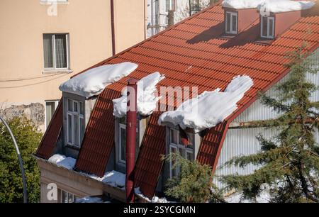 Heavy snow on rooftops in Batumi melting under the sun, creating dangerous icicles and risks of roof collapse. Snowfall in warm climate causing damage to cars and pedestrians. Stock Photo