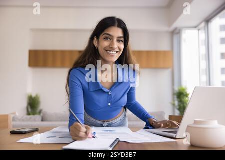 Indian woman working leaning over desk with papers and laptop Stock Photo
