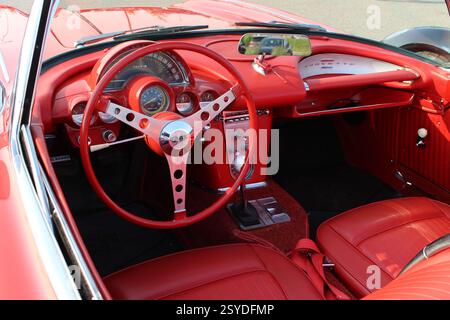 Interior of a classic red sports car featuring chrome steering wheel, vintage gauges, and red leather upholstery. Stock Photo