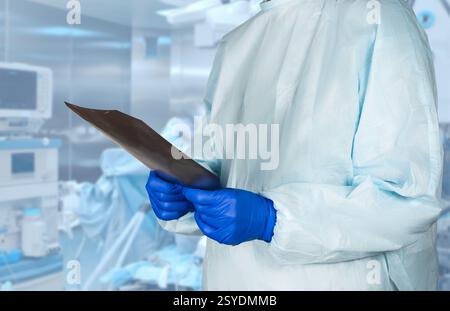 A medical professional wearing protective clothing observes X-rays in a sterile surgical setting, ensuring patient care and safety. Stock Photo