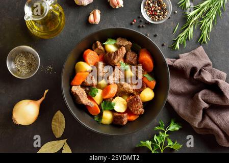 Beef stew with potatoes, carrots and greens in black bowl on dark stone background. Comfort healthy food for dinner. Top view, flat lay Stock Photo