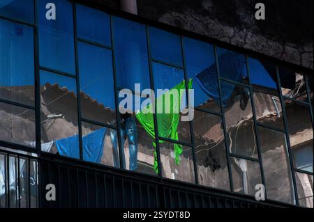 The lime green dressing gown: mirror glass in commercial building in Catania, Sicily, Italy, reflects high level washing lines strung across courtyard on opposite side of narrow street.  Family laundry includes two dressing gowns or robes, a pair of ripped jeans, two towels and a string vest. Stock Photo