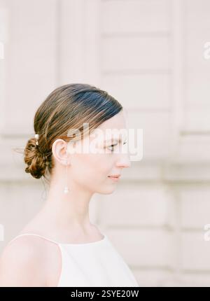 Woman with a sleek bun hairstyle showcases elegance in a minimalist setting during daylight hours. Stock Photo