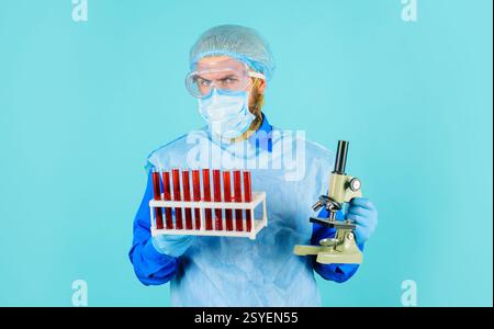 Doctor with blood samples in test tubes and microscope. Blood test in laboratory. Professional scientist or lab assistant in medical mask, safety glas Stock Photo