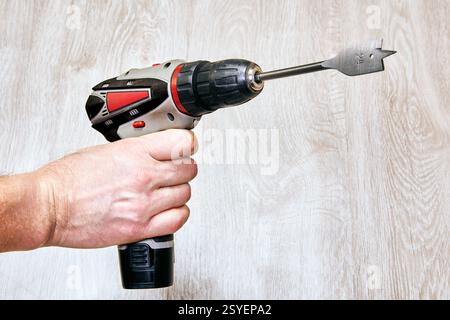 Cordless drill with spade bit held by hand. Stock Photo
