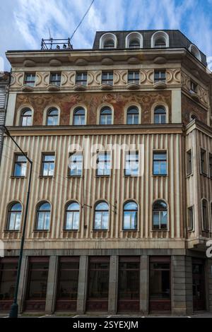 A multi-story building with a decorated facade featuring rows of arched windows, contrasting textures, and a dark-colored upper level under a cloudy s Stock Photo