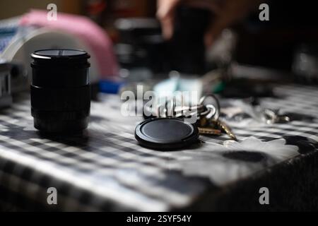 A close-up reveals various camera lenses and accessories scattered on a checkered tablecloth, with a set of keys resting prominently to the side, hint Stock Photo