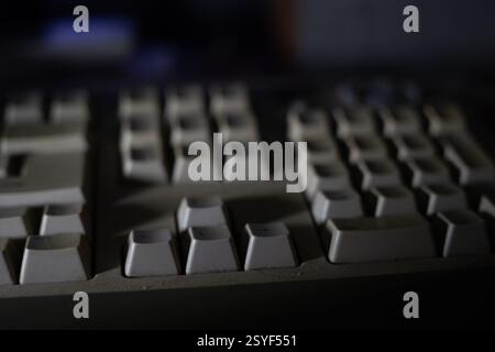 This close-up view captures a vintage computer keyboard covered in dust against a dimly lit background. The worn keys suggest years of usage during la Stock Photo