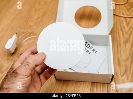 Paris, France - Jun 17, 2021: A person holds the white IKEA TRADFRI smart hub above its open packaging on a wooden surface, with a power adapter, manu Stock Photo