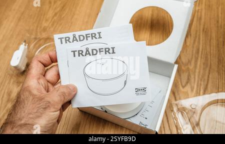 Paris, France - Jun 17, 2021: A person holds IKEA TRADFRI instruction manuals while unboxing a smart home hub, with the packaging, adapter, and device Stock Photo