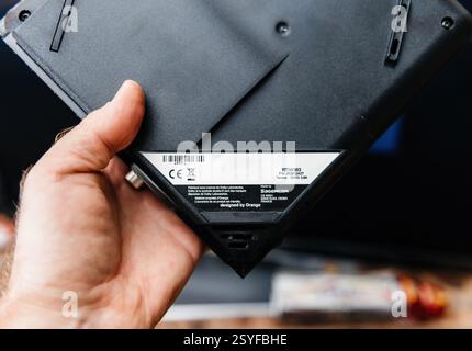 Paris, France - Feb 17, 2025: A person holds an older model of an Orange TV decoder by Sagemcom, showcasing its black plastic casing, technical specif Stock Photo