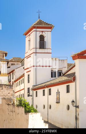 Granada town in Spain. Whitewashed building with red trim and bell tower against a vibrant blue sky. A charming architectural detail in a sunny, histo Stock Photo