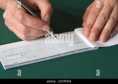 Closeup woman's hands writing bank cheque on green background Stock Photo