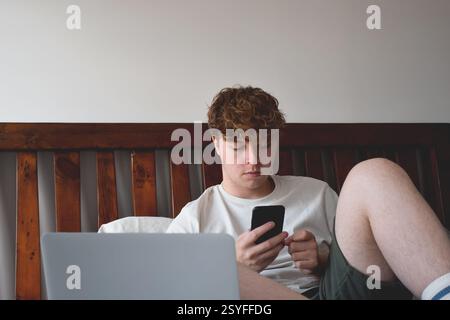 Young man sitting on bed using mobile phone Stock Photo