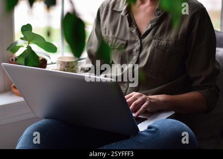 Woman sitting by a window at home using laptop computer Stock Photo