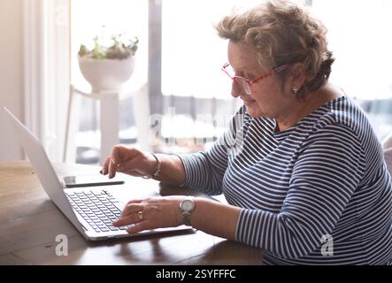 Senior woman sitting at table using laptop computer Stock Photo