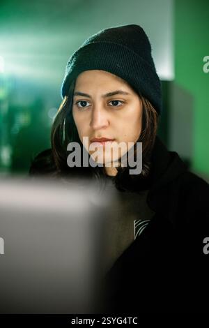 Female young hacker working on computer in dark room programming code Stock Photo