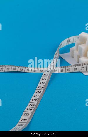 A roll of measuring tape is laid out alongside sugar cubes on a bright blue surface. The measuring tape displays numbers, indicating precise measureme Stock Photo