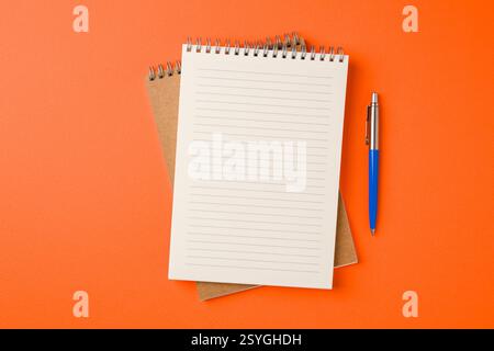 Top view of notebook and ballpoint pen on orange background Stock Photo