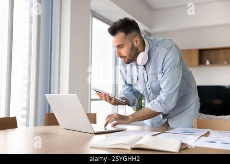 Man standing at desk, focused on his work on laptop Stock Photo