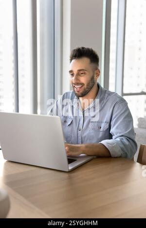Smiling man sitting at desk working on studying using laptop Stock Photo