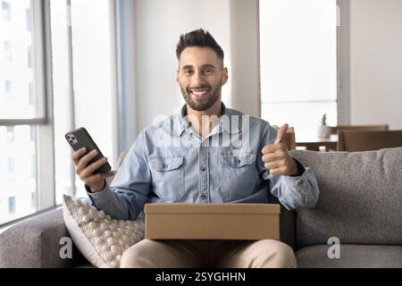 Man holds phone and box smiling at camera, showing thumbs-up Stock Photo