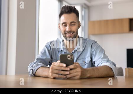 Hispanic man using his smartphone seated at table at home Stock Photo