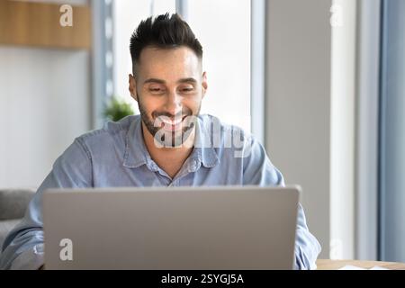 Smiling Latin man using laptop at home office Stock Photo