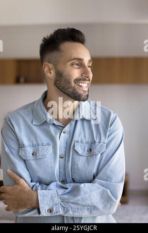 Pensive Hispanic man standing in cozy domestic space with arms-crossed Stock Photo