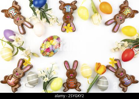 Frame made of colourfully decorated Easter bunnies, Easter eggs and flowers on a white background Stock Photo