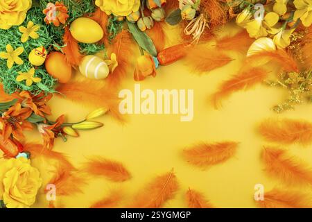 Orange feathers and flowers with Easter eggs on a yellow background Stock Photo