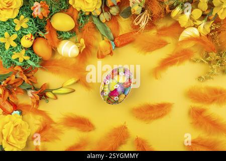 Orange feathers and flowers with Easter eggs on a yellow background Stock Photo