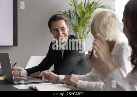Smiling businessman sit by notebook listen to colleagues at boardroom Stock Photo
