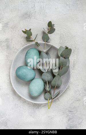 Easter colored eggs, in turquoise tones, on a gray plate, with a branch of eucalyptus, Easter card, top view, no people Stock Photo