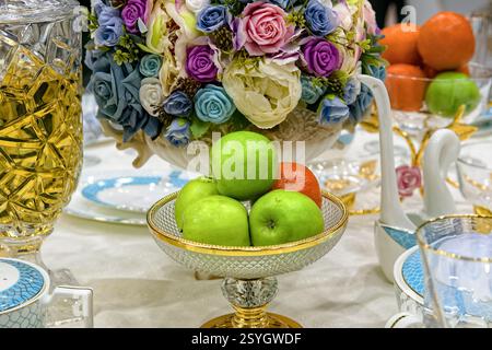 Fresh fruits in glass vase on festively decorated table. Stock Photo