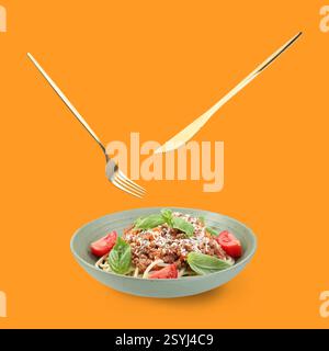 Cutlery in air over plate with tasty pasta bolognese on orange background Stock Photo