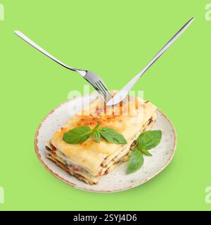 Cutlery in air over plate with tasty lasagna on light green background Stock Photo