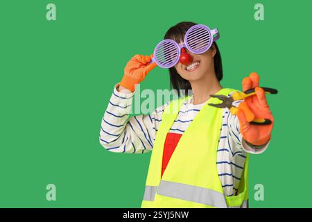 Young smiling female builder with pliers on green background. Fool's day Stock Photo