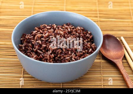 Healthy cooked brown rice mixed with riceberry in a grey ceramic bowl with a wooden spoon and bamboo chopsticks. Stock Photo