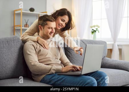 Happy family, young spouses, smiling couple in love using computer laptop together at home, talking Stock Photo