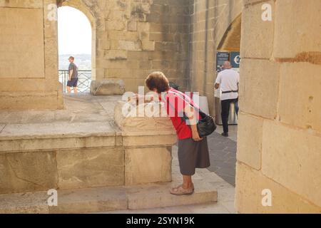 Senior woman petting stray ginger cat in public park in Valletta, Malta Stock Photo